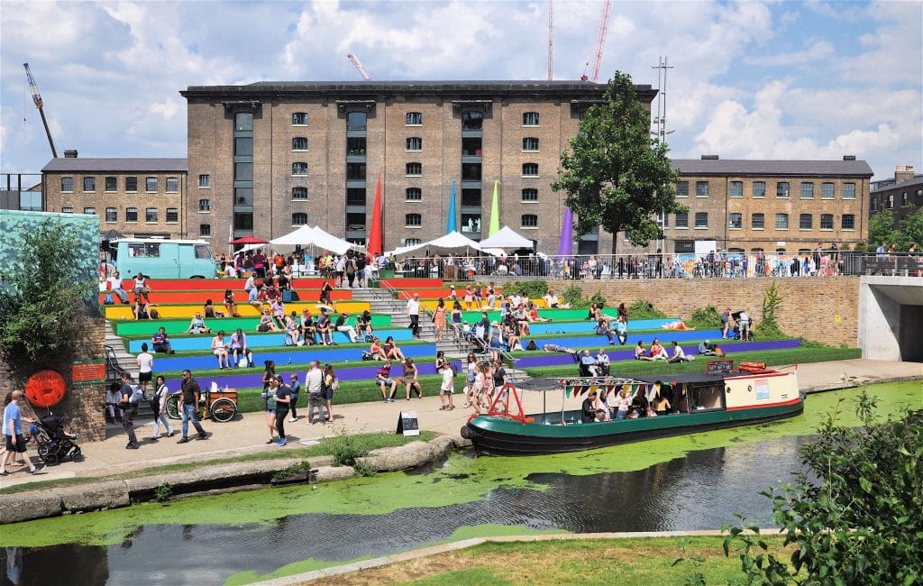 Outside Queer Britain Museum, LGBTQ+ individuals gather on a field with large rainbow stairs. This is where Charity Queer Britain established its first physical home in Granary Square on May 5, 2022, marking the opening date of the UK's first LGBTQ+ Museum.