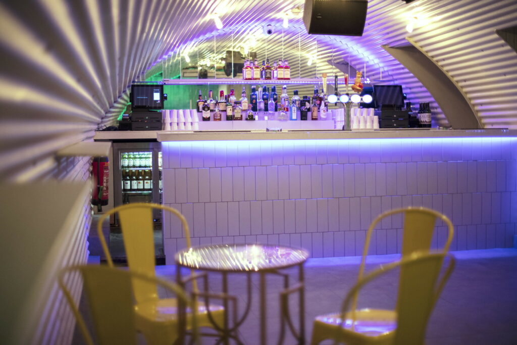 Interior of She Soho: Purple light fills the space, illuminating yellow chairs beneath a white curved ceiling.