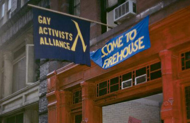 Exterior of the Gay Activists Alliance Firehouse, the organization's headquarters from 1971 to 1974. Flags display text: 'Gay Activists Alliance' and 'Come to firehouse.