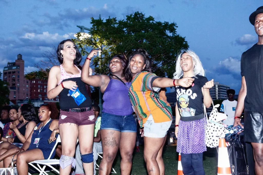 A vibrant scene at the Kiki Youth Pride Festival, with a group of queer women joyfully dancing at The Christopher Street Pier in New York City.