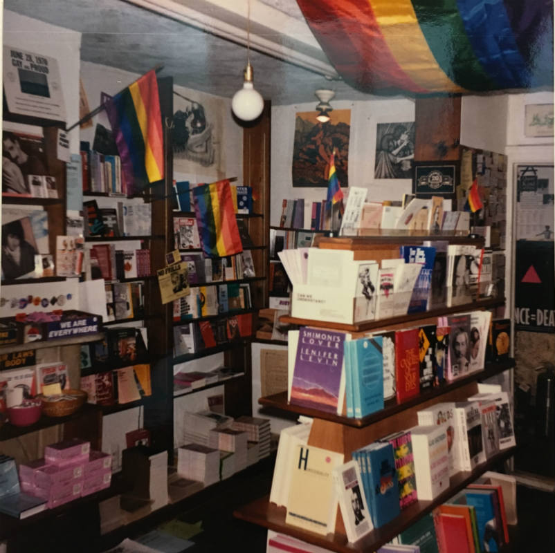 Interior of The Oscar Wilde Memorial Bookshop, the first instance in American history where literature was organized under the subject heading of gay culture. Pride flags adorn the shelves filled with books.