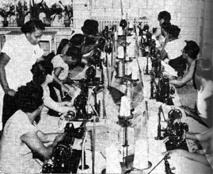 Black and white photo from 1955 showing women inside the Women's House of Detention. The women are engaged in practical instruction, working with power sewing machinery despite limited space and equipment.