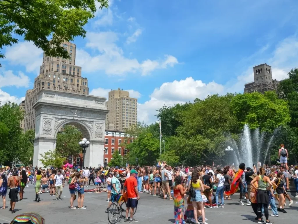A vibrant scene in Washington Square Park, with people of all ages and backgrounds joyously celebrating Pride.