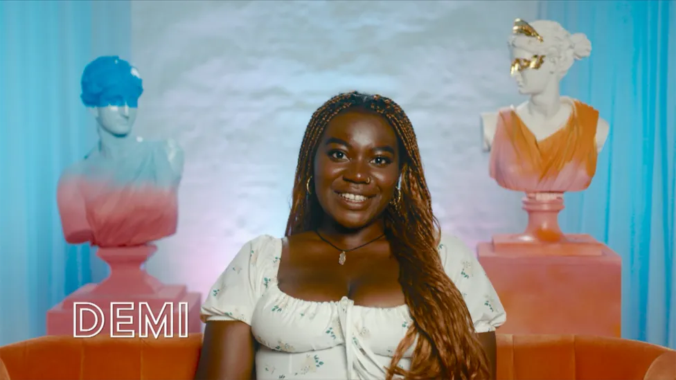 Portrait of Demi, a character from the BBC's 'I Kissed a Girl' TV show, aged 23. She is wearing a white dress adorned with small flowers. Demi uses she/her pronouns and works as a Publishing Executive. From: Hemel Hempstead.