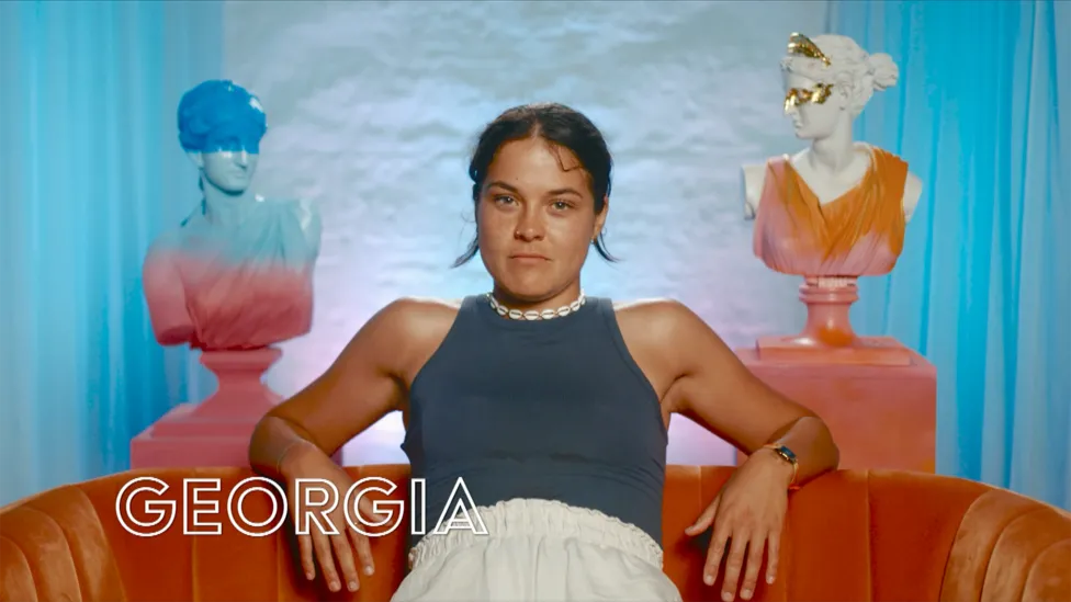 Georgia, 28 (She/Her), confidently seated, wearing a dark blue top and white pants. From Hunmanby, North Yorkshire. Occupation: Professional Footballer.
