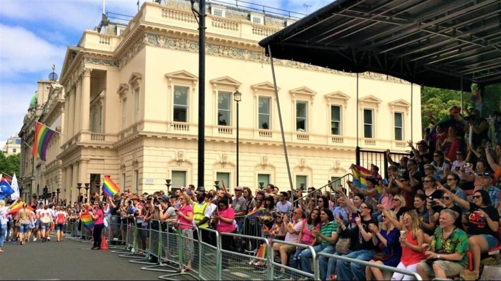 A group of LGBT people sit on the grandstand at the Pride in London 2024 Parade on Piccadilly, surrounded by rainbow flags, celebrating one of the London Pride events 2024.