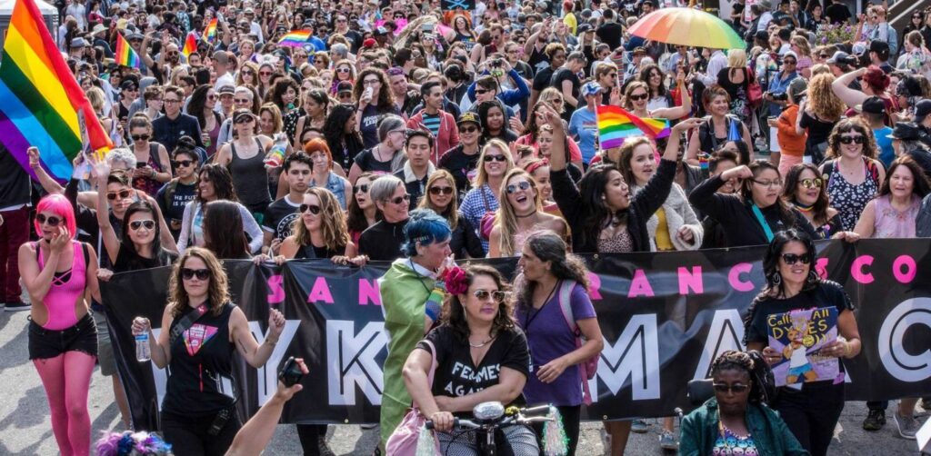 A vibrant crowd fills the streets, waving rainbow flags and cheering enthusiastically. This lively scene captures the spirit of The San Francisco Dyke March 2023. Participants celebrate diversity, unity, and LGBTQ+ rights in a colorful display of solidarity and joy.