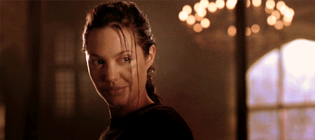 Angelina Jolie as Lara Croft in 'Tomb Raider,' smiling confidently with strands of her front hair playfully blowing around her face.