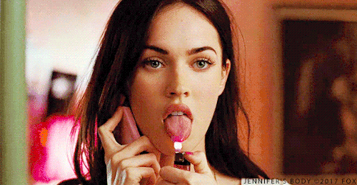 Megan Fox from the movie Jennifer's Body, illuminated by a fiery glow as she lights up her tongue with a lighter.