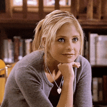 Scene from Buffy the Vampire Slayer: A blonde woman in a gray sweater and a heart-shaped necklace