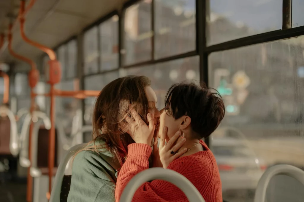 Two women kissing in a public bus. Both of them are wearing rings and accessories that reflect their own personal gender presentation.
