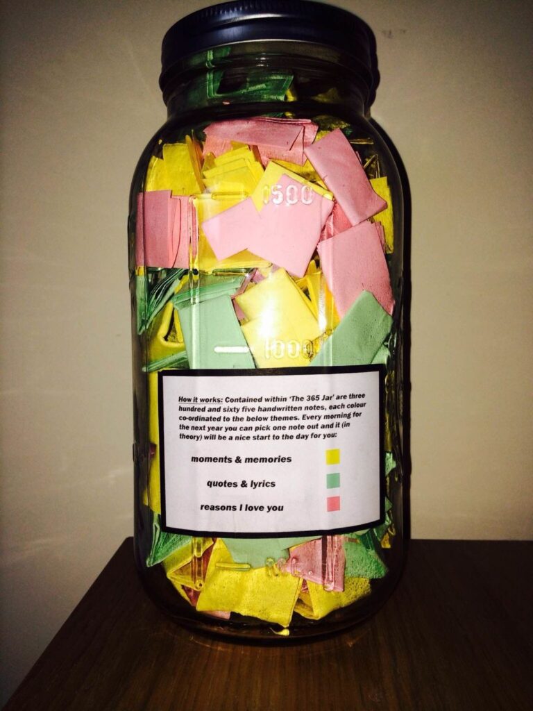 A jar filled with colorful folded notes labeled "The 365 Jar" contains handwritten messages organized by themes—moments and memories, quotes and lyrics, and reasons I love you—designed for daily inspiration throughout the year.